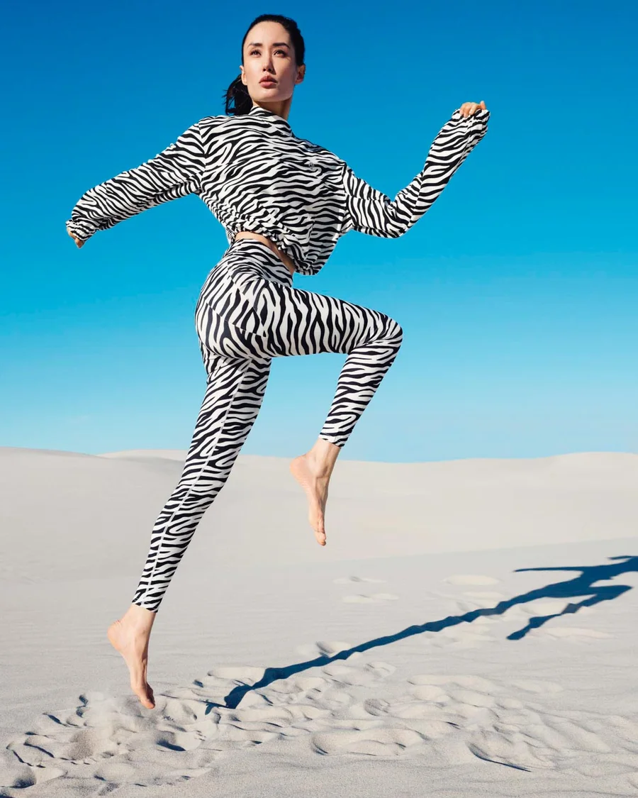 Frau im Zebra-Catsuit springt auf weißem Sand