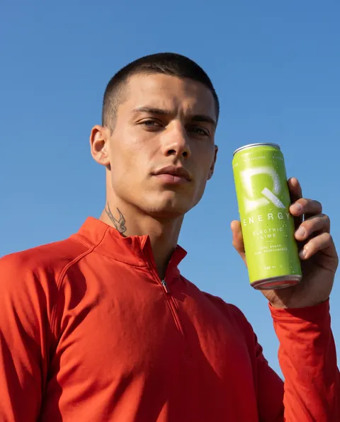 Quinn hält eine Dose DQ Energy Electric Lime vor blauem Himmel